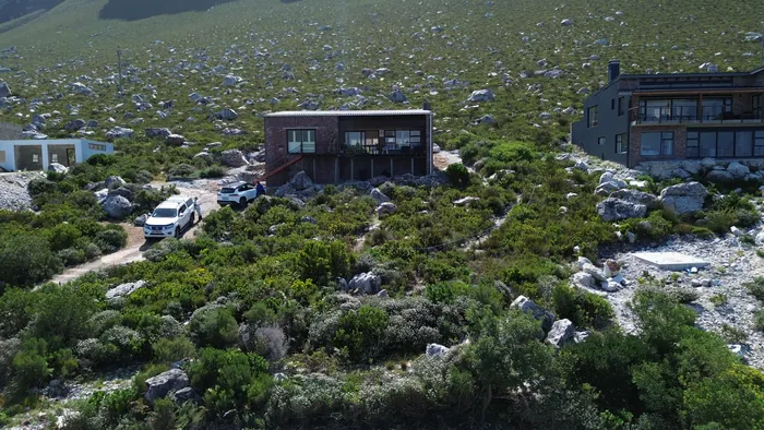 The house in its setting, granite boulders and low fynbos running up the slope behind it
