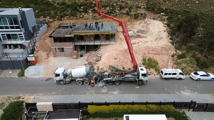 The concrete pump and readymix truck standing in the road, with the boom reaching over the house to the crew on the slab