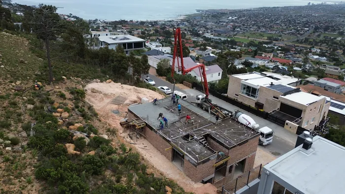 The house at two storeys with the second floor slab being cast, the bay and the town behind it